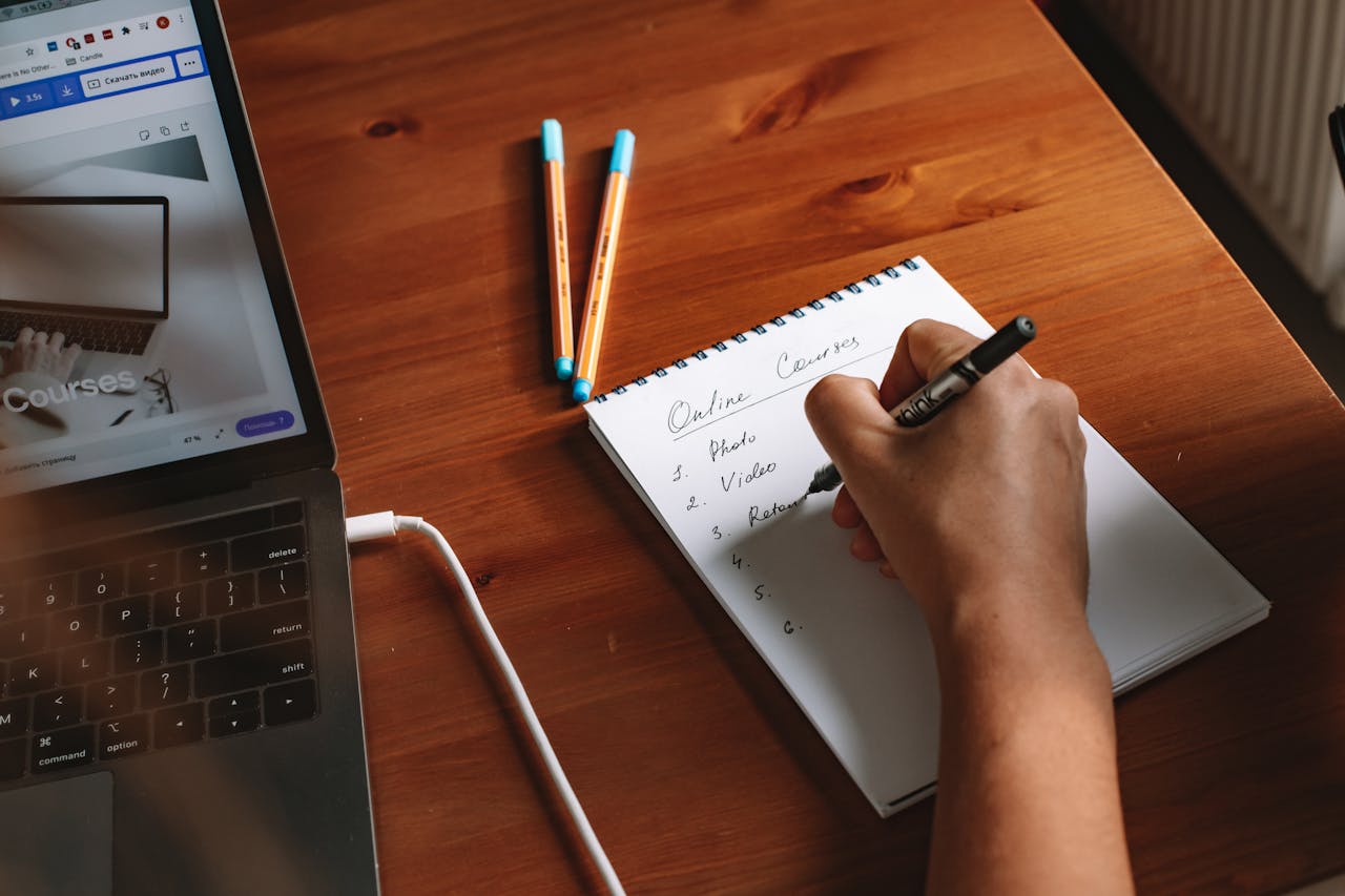 Photo of a person writing a list of online courses on a notepad next to a laptop.